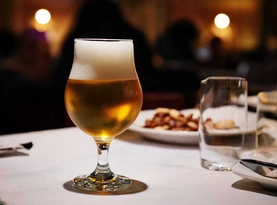 Gyllent pilsner med tett skum i tulipanglass på hvit duk